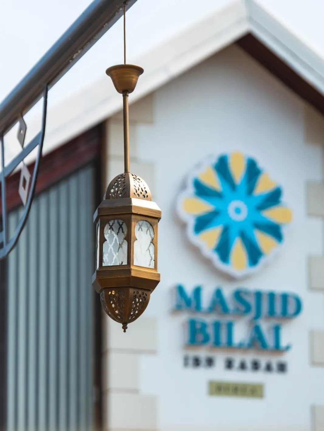 A brass lantern in front of the Masjid Bilal Ibn Rabah signage